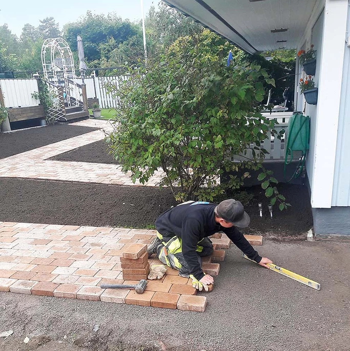 Man i mörka arbetskläder som lägger stenplattor